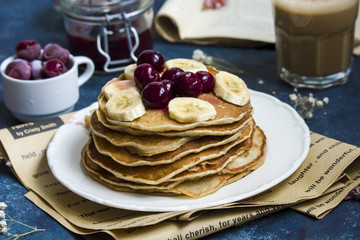 Pancakes with banana and cherries on the top and a cup of coffee
