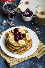 Pancakes with banana and cherries on the top and a cup of coffee