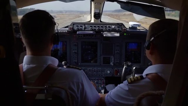 Shot of two pilots in a cockpit flying a plane, taking off from the ground.
