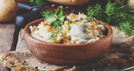 Traditional Russian vareniki with potatoes and fried onions in bowl on old wooden table, rustic style, selective focus