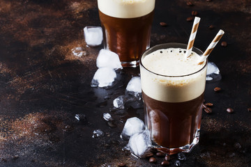 Cold frappe coffee with ice and foam in large glasses on brown background, selective focus
