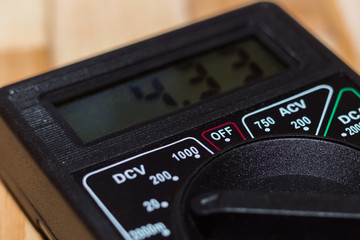 Digital measuring multimeter on wooden floor. It shows 4.33V or fully charged battery. Includes voltmeter, ampermeter, ohmmeter.