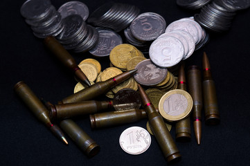 One euro, Russian ruble and small Ukrainian coins with rifle military ammo on black background....