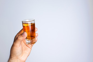 A man's hand holds a glass with liquid on a gray background