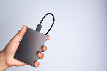 A man's hand holds a portable hard drive on a gray background