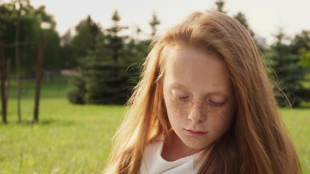 Gloomy face of sad ginger little girl with freckles with lowered eyes