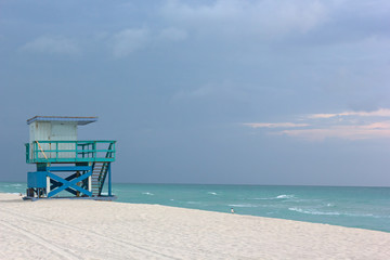 Lifeguard cabin on empty Miami Beach at cloudy sunrise. Seagulls on a sandy sea beach and lonely cabin near the water edge with a lifeguard off duty.