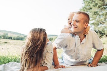 Young Adult Couple with Their Little Daughter Having Fun in the Park Outside the City, Family Weekend Picnic Concept, Three People Enjoying Summer Time