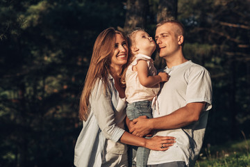 Fototapeta premium Young Adult Couple with Their Little Daughter Having Fun in the Park Outside the City, Family Weekend Picnic Concept, Three People Enjoying Summer Time