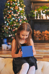 Obraz premium curious little girl smiling while opening Christmas presents. Beautifully decorated Christmas tree and house with lights and lantern.