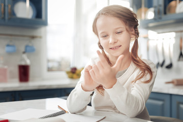 Express positivity. Cheerful schoolgirl keeping smile on her face while looking at her fingers
