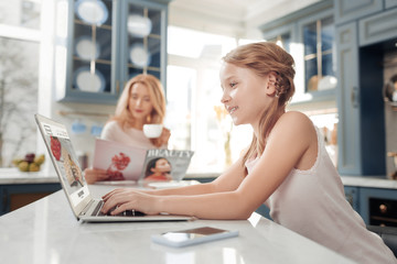 Morning interaction. Attractive little female sitting in semi position and looking at screen of her...