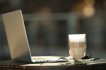 Hot art Latte Coffee in a cup on wooden table and and laptop in coffee shop blur background with bokeh image.