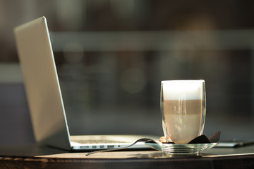 Hot art Latte Coffee in a cup on wooden table and and laptop in coffee shop blur background with bokeh image.