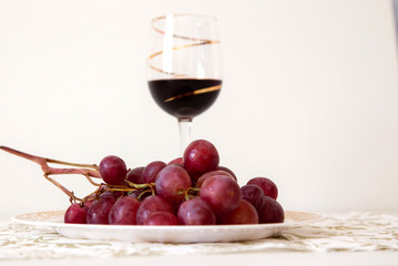 bunch of red grapes with a glass of red wine in the background