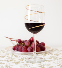 golden glass of red wine with red grapes at background