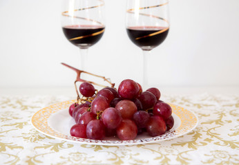 golden plate with red grapes and two glasses of red wine at background