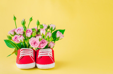 Baby shoes with rose flowers on yellow background with copy space