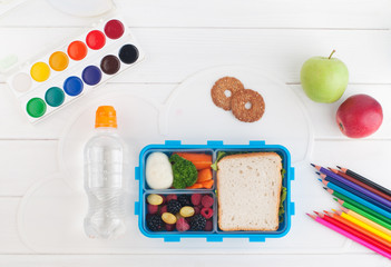Open school lunch box near water bottle on the white wooden background
