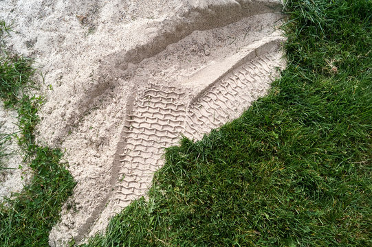 Tire tracks in the sand that was placed over the green grass during construction