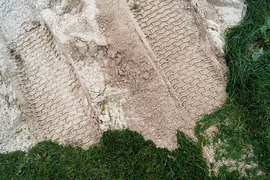 Tire tracks in the sand that was placed over the green grass during construction