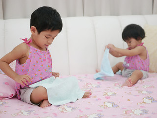 Little Asian baby girl, 32 months old, (left) learning to fold clothes - baby's development through...