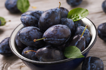 Full bowl of freshly harvested ripe prune fruits on a wooden table, close-up