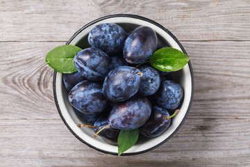 Top view of a bowl full of ripe prune fruit on a wooden table