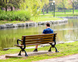 Man Sitting On A Park Bench Near A River With Trees In The Background