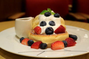 Front View of Fluffy Souffle Pancake with Fresh Whipped Cream and Mix Berries on White Plate with Syrup Pitcher 