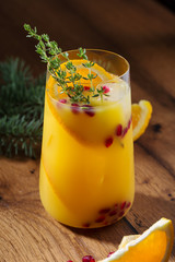 Winter orange cocktail with pomegranate seeds. On wooden table, with christmas tree branches, in glasses. Copy space