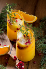 Winter orange cocktail with pomegranate seeds. On wooden table, with christmas tree branches, in glasses. Copy space