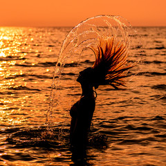 Teen Girl In A Dress With Long Hair At The Beach In Silhouette During Sunset Flipping Her Hair In The Water