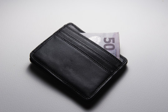 A black leather wallet on a white background with the corner of a NZ$50 note sticking out of the top.