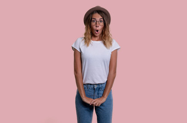 Young girl with long hair in a hat stands on an isolated pink background. She opened her mouth in surprise.