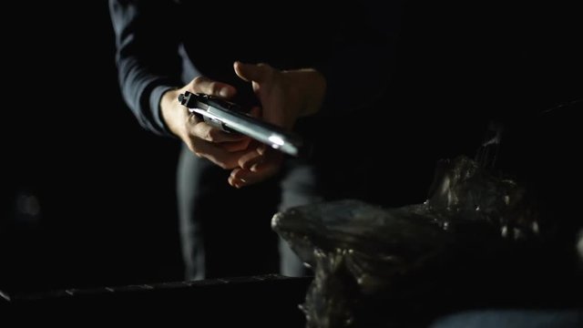Hitman in hoodie taking handgun from car trunk, serial killer, contract crime