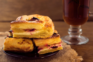 Dessert of cut into pieces cake with cottage cheese and plums, tea with mint in a glass, wooden background.