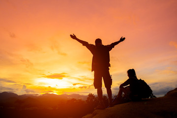 Hikers with backpacks standing on top of a mountain and enjoying sunrise