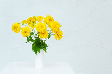 A bouquet of yellow flowers Heliopsis in a white vase. In a room on a white dresser.