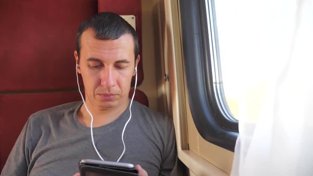 man listening lifestyle to the music on the train rail car coupe compartment travel. slow motion video. man with a smartphone at the window of a train in a car travel internet social media web. man