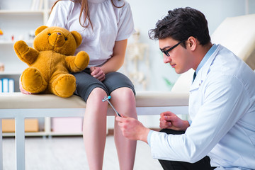 Doctor checking up young girls reflexes with hammer
