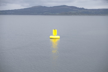 Yellow buoy bright light in open sea under dark grey clouds and mountain