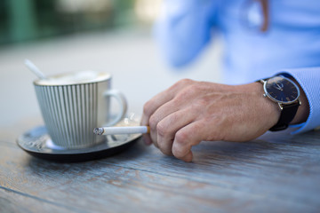 Closeup shot of a cup of coffee and a mans hand with a cigarette