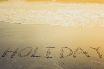 Holiday handwriting on sand beach with sand scoop toy next to the waterline with sunlight on the morning.