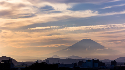 Fototapeta na wymiar Mount Fuji surrounded by misty clouds before sunset, looming over a small city
