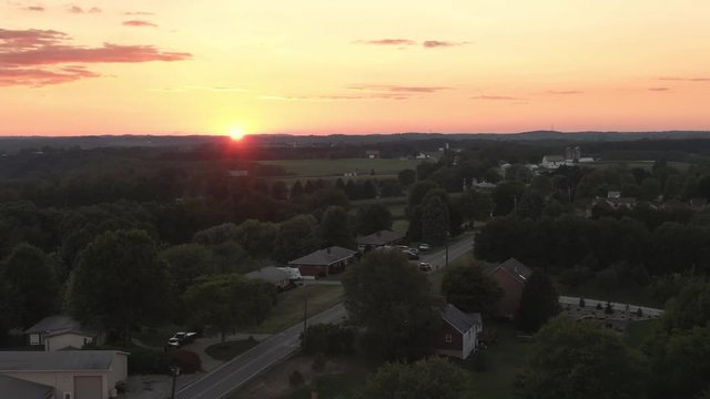 A slow reverse aerial establishing shot view of a western Pennsylvania sunset over a small countryside residential neighborhood. Pittsburgh suburbs.  	