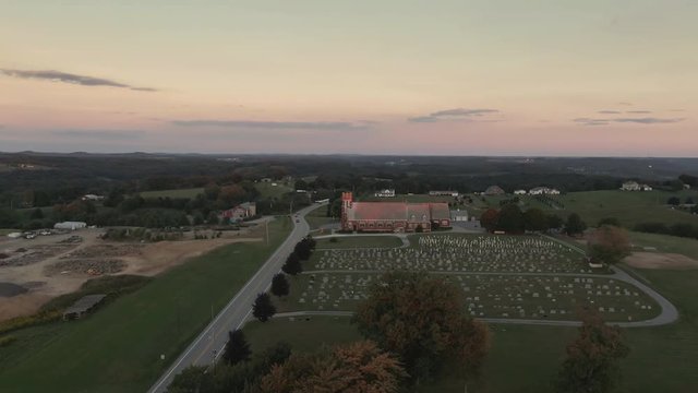 A high angle orbiting establishing shot of a church in the western Pennsylvania countryside at sunset. Pittsburgh suburbs.  	