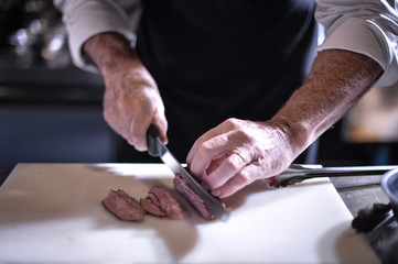 chef with knife and cutting tasty grilled steak, Chef preparing food, meal, in the kitchen.