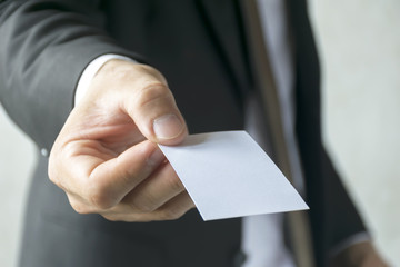 Businessman holding a white business card. Black suit.