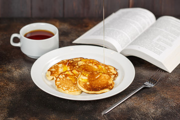 Pancakes with honey on white plate, tea and book